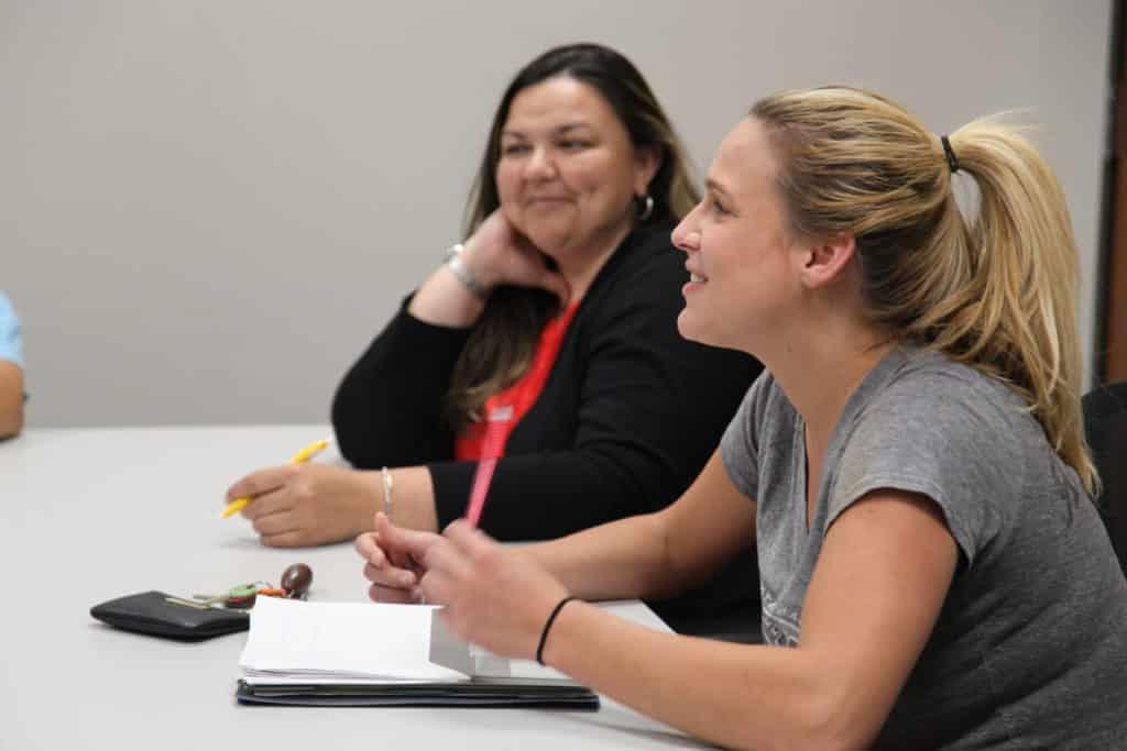 Two women engaged in a discussion at a Howard Payne University meeting, with notepads and pens on the table. | HPU